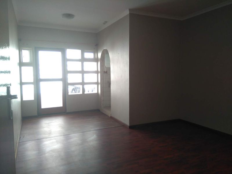 An empty living room featuring dark laminate flooring, an arched entryway, and natural light entering through a multi-pane glass door and windows.