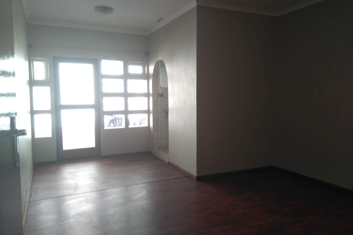 An empty living room featuring dark laminate flooring, an arched entryway, and natural light entering through a multi-pane glass door and windows.
