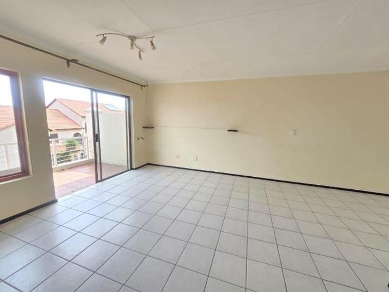 Spacious, empty living area featuring neutral tiled flooring and a large sliding glass door providing access to an outdoor balcony.