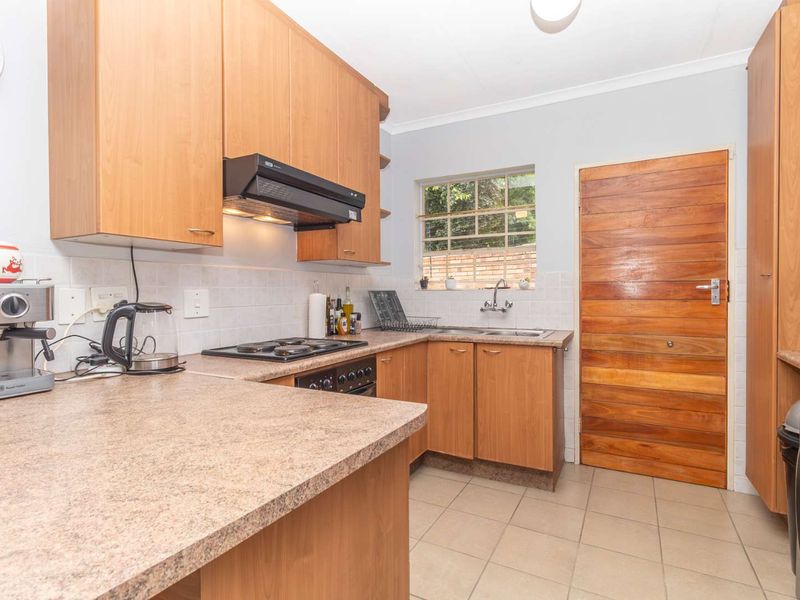 Functional kitchen featuring laminate cabinetry, laminate countertops, built-in oven, electric hob, extractor fan, double sink, and tiled flooring with a timber door.