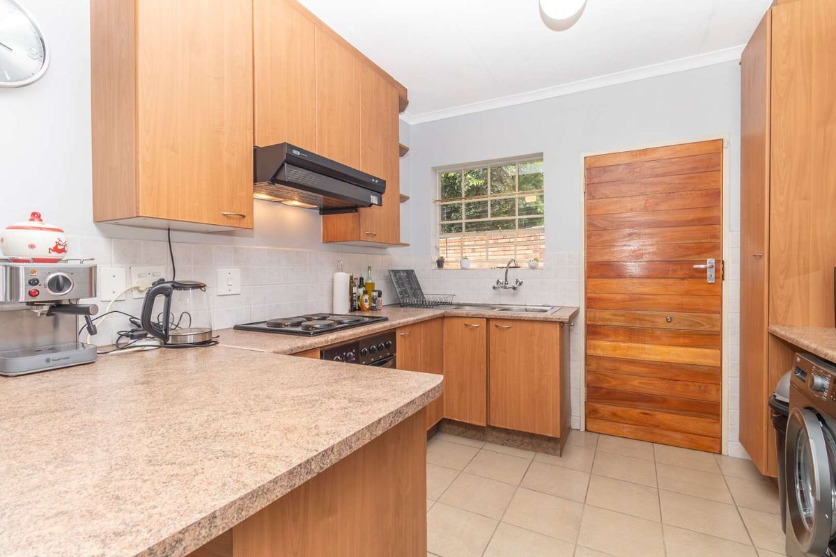 Functional kitchen featuring laminate cabinetry, laminate countertops, built-in oven, electric hob, extractor fan, double sink, and tiled flooring with a timber door.