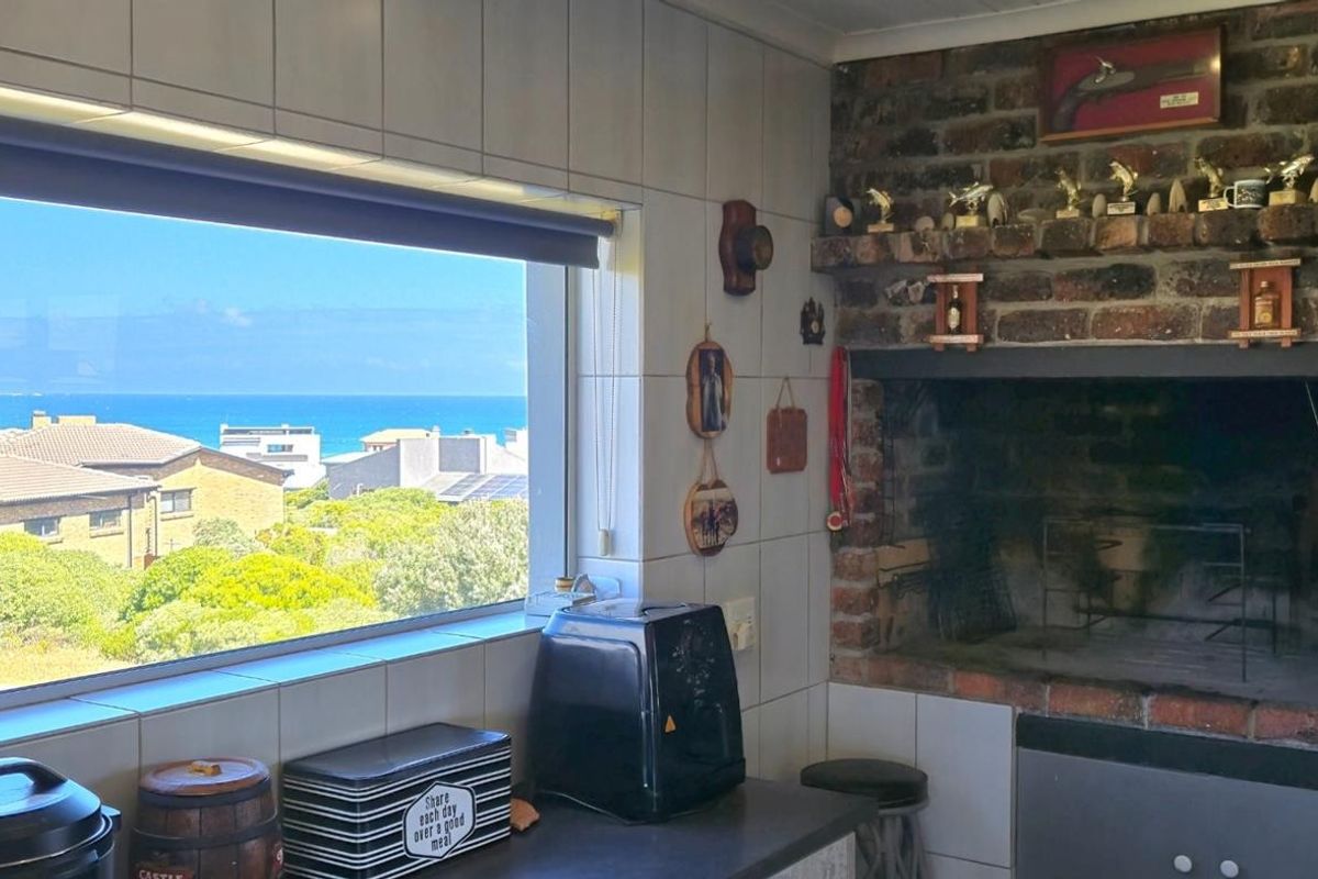 Indoor braai area featuring a built-in brick fireplace, tiled surfaces, and a large window offering scenic coastal views.