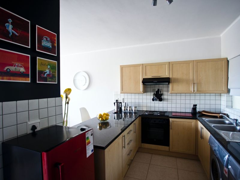 A functional kitchen featuring light wood cabinetry, black granite countertops, a tiled backsplash, and integrated appliances including an oven and hob.