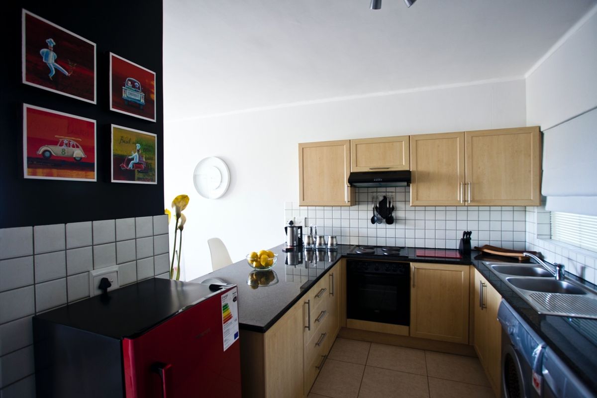 A functional kitchen featuring light wood cabinetry, black granite countertops, a tiled backsplash, and integrated appliances including an oven and hob.