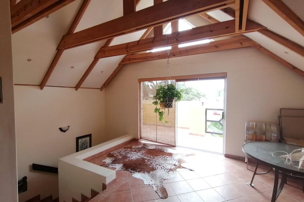 Spacious living area featuring high vaulted ceilings with exposed timber beams, tiled flooring, and large sliding glass doors leading to an outdoor balcony.