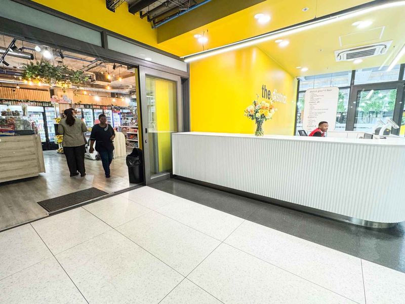 Modern commercial building entrance featuring a bright yellow accent wall, a sleek white reception desk, and polished tiled flooring.