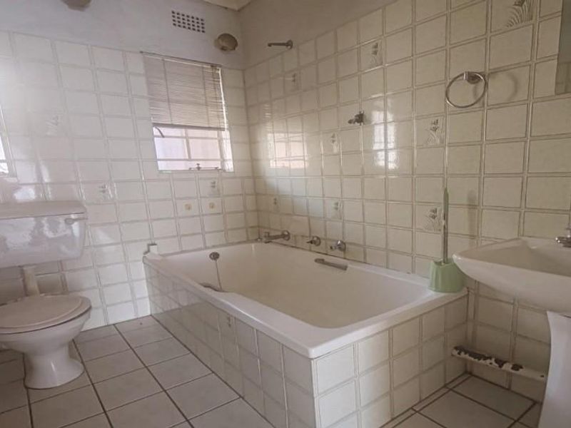 A dated bathroom featuring a pedestal basin, built-in bathtub, and toilet, finished with original wall and floor tiling.