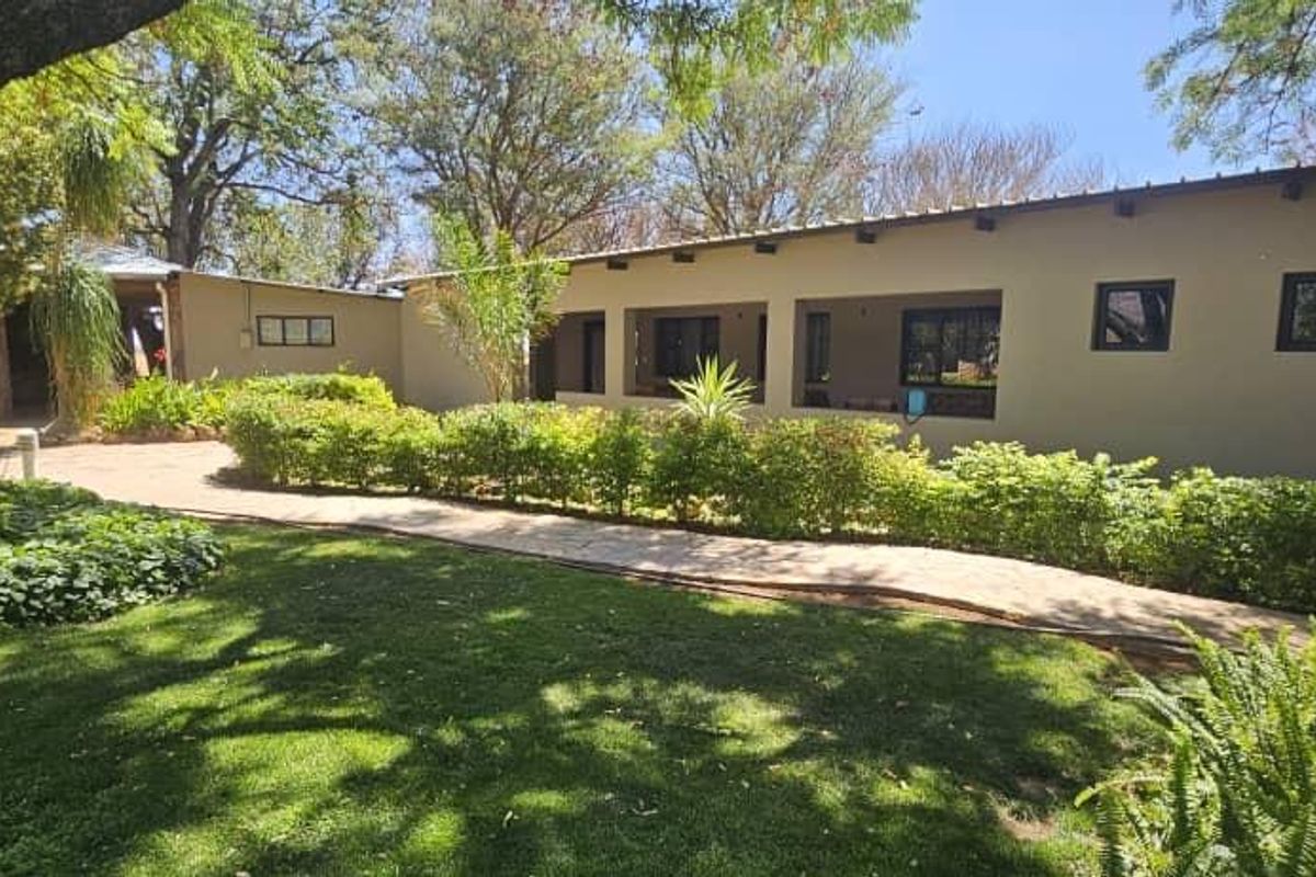 Rear view of the property featuring a covered patio area, paved walkway, and well-maintained garden with mature trees.