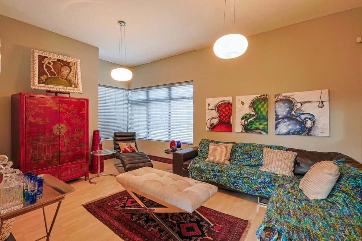 A living room featuring light wood-look flooring, large windows with fitted blinds, and modern pendant lighting.