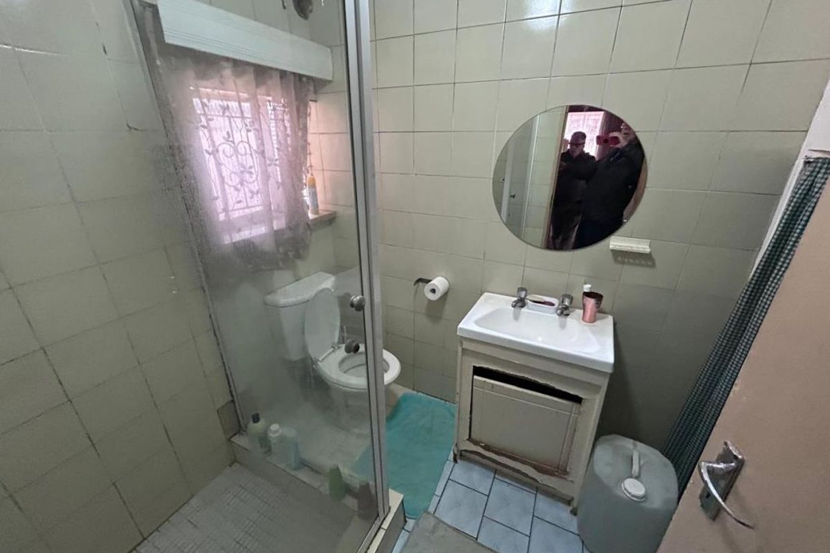 Compact bathroom featuring a shower enclosure, toilet, and vanity basin with dated wall and floor tiling.