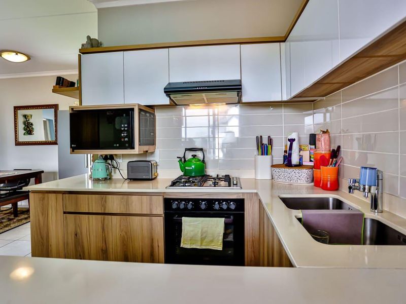 Modern kitchen featuring wood-finish cabinetry, white upper cabinets, gas hob, built-in oven, extractor fan, and a double sink with tiled backsplash.