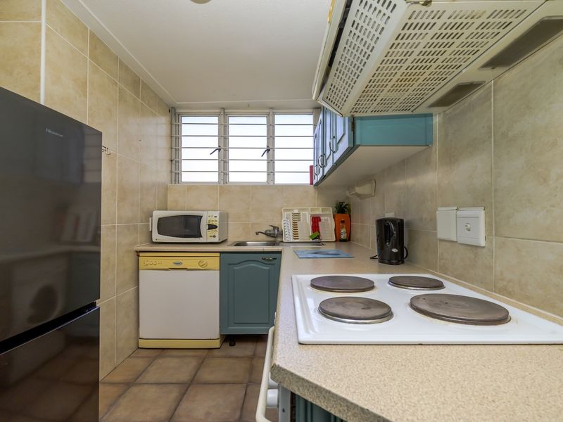 A compact kitchen featuring tiled walls and flooring, built-in cabinetry, a stainless steel sink, and an electric hob with an overhead extractor fan.