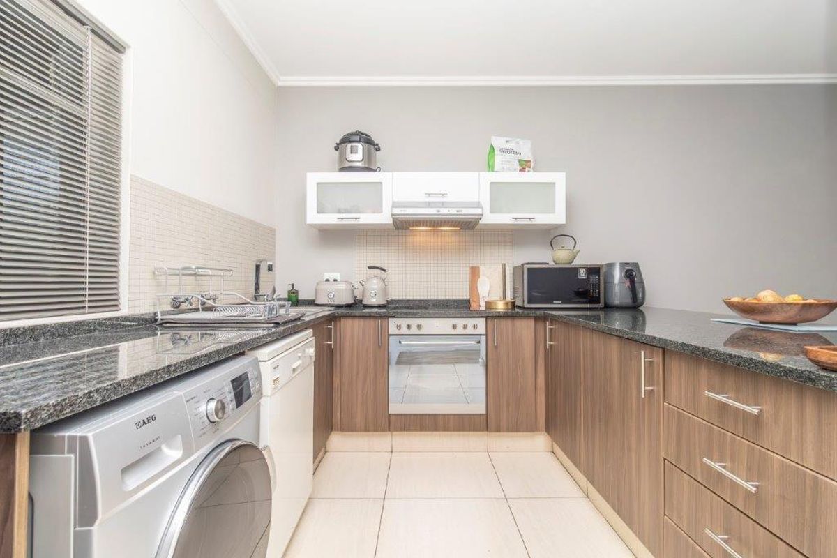 A functional kitchen featuring wood-finish cabinetry, granite countertops, tiled backsplash, and integrated space for laundry appliances.