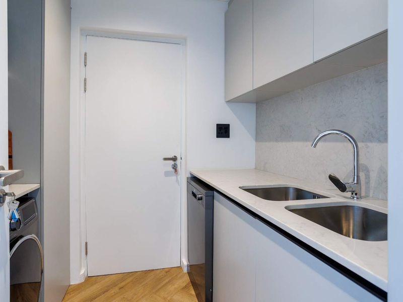 A modern, compact scullery featuring sleek cabinetry, stone countertops, a double stainless steel sink, and integrated dishwasher, finished with herringbone wood flooring.