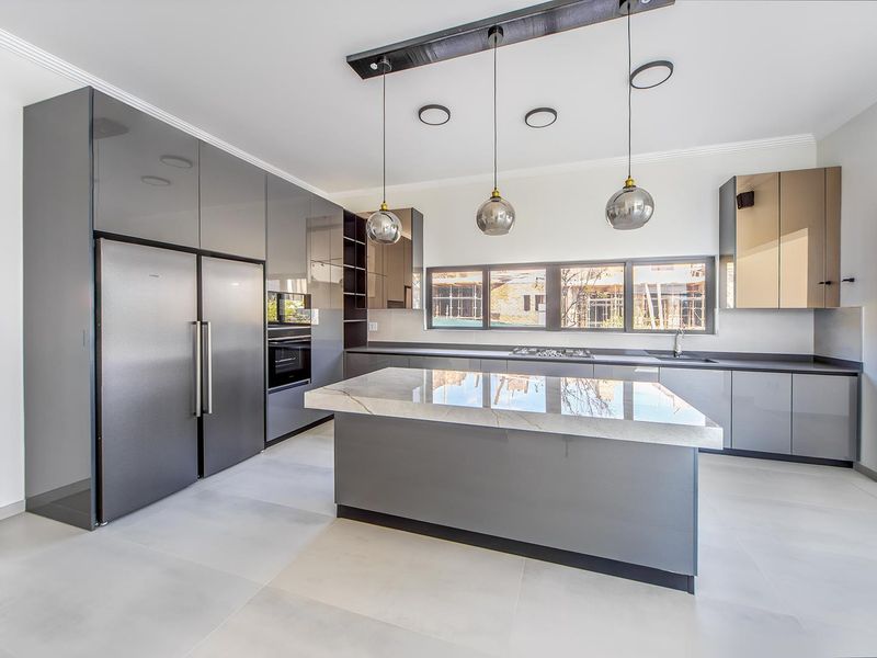 Modern kitchen featuring high-gloss grey cabinetry, a central stone-topped island, integrated appliances, and contemporary pendant lighting in a clean, minimalist space.