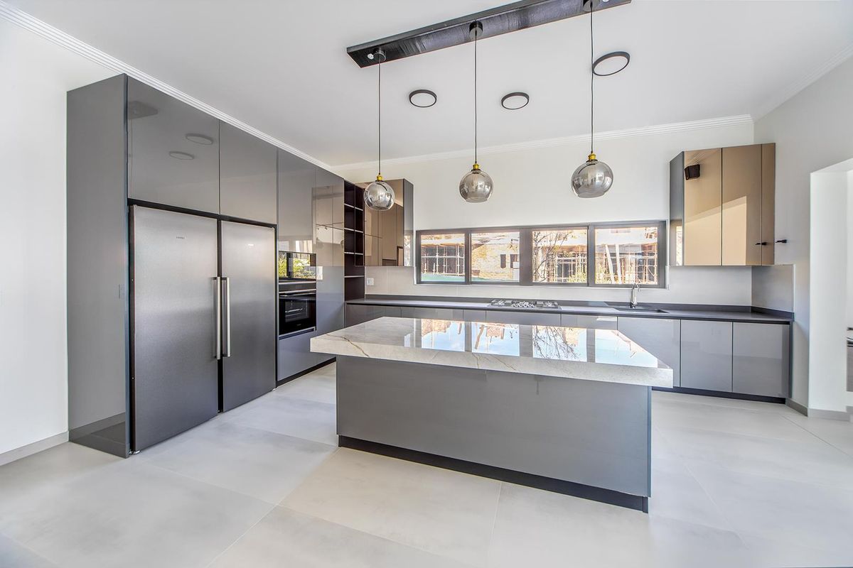 Modern kitchen featuring high-gloss grey cabinetry, a central stone-topped island, integrated appliances, and contemporary pendant lighting in a clean, minimalist space.