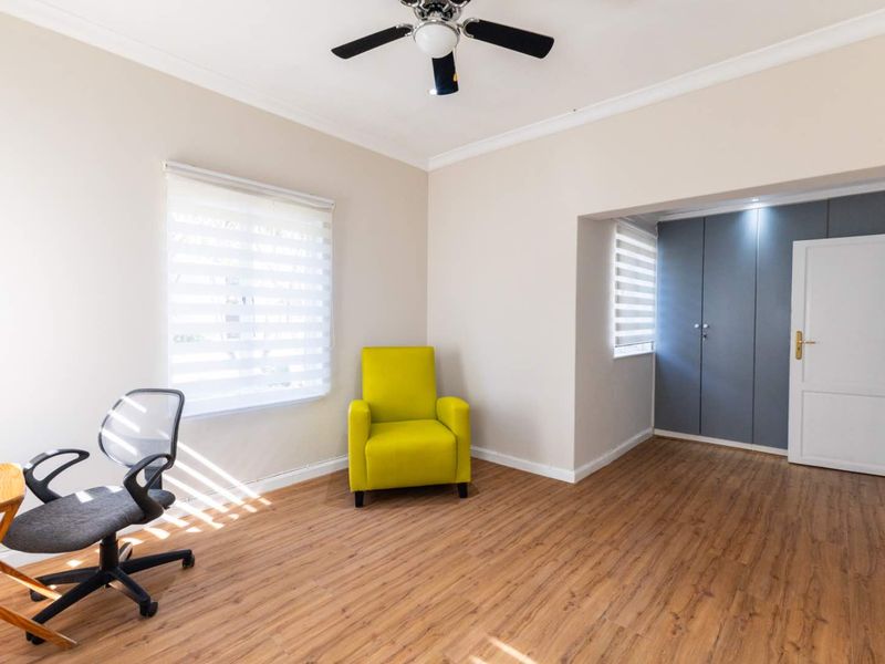 A bright bedroom featuring laminate flooring, built-in cupboards, a ceiling fan, and neutral wall tones, offering a clean and functional living space.