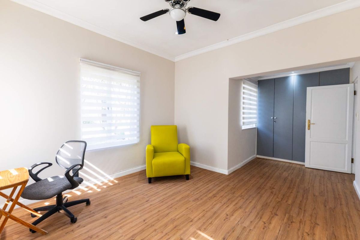 A bright bedroom featuring laminate flooring, built-in cupboards, a ceiling fan, and neutral wall tones, offering a clean and functional living space.