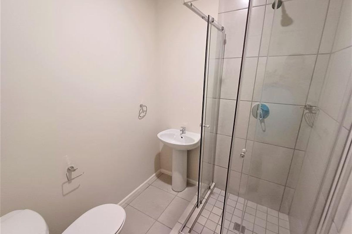 A functional bathroom featuring a pedestal basin, a glass-enclosed shower with tiled walls, and a standard toilet.