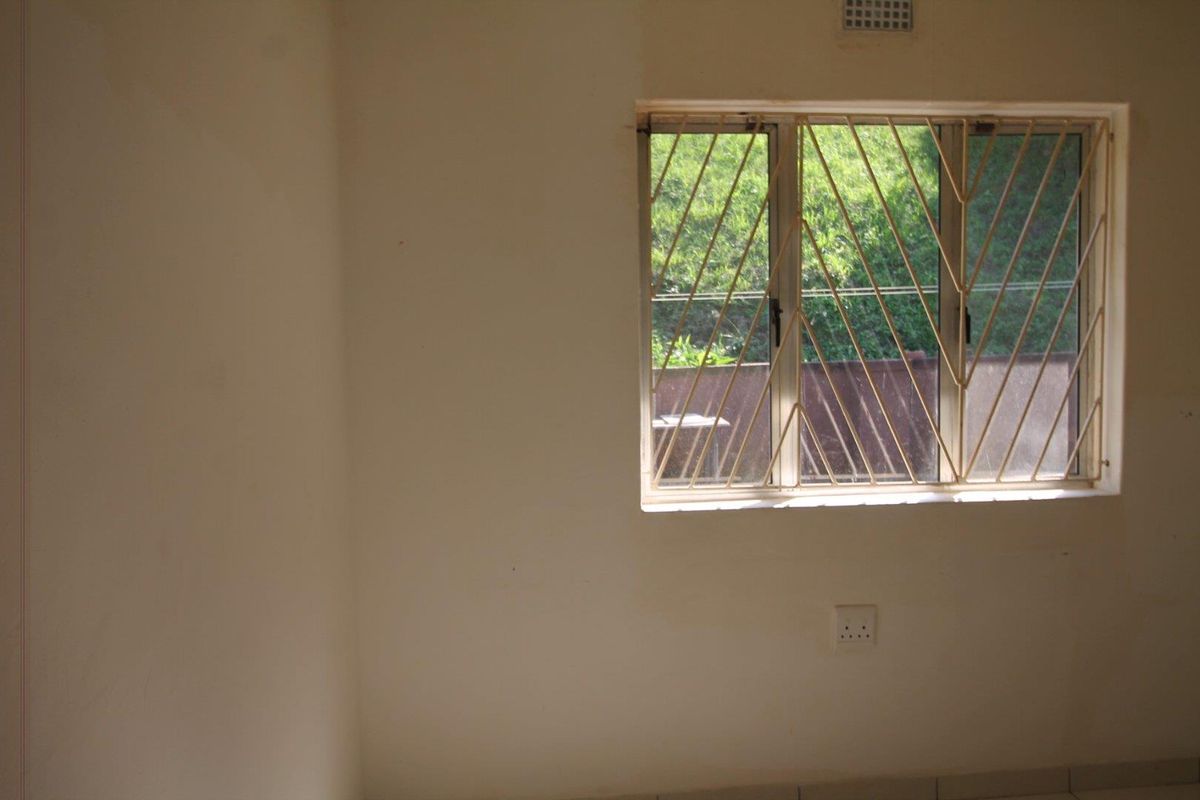 A vacant bedroom featuring a window with integrated security bars and a wall-mounted electrical outlet.