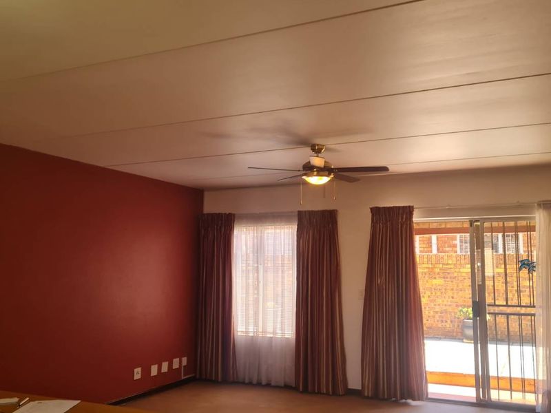 Spacious living area featuring a ceiling fan, carpeted flooring, and direct access to an outdoor patio through a sliding glass door with security gate.