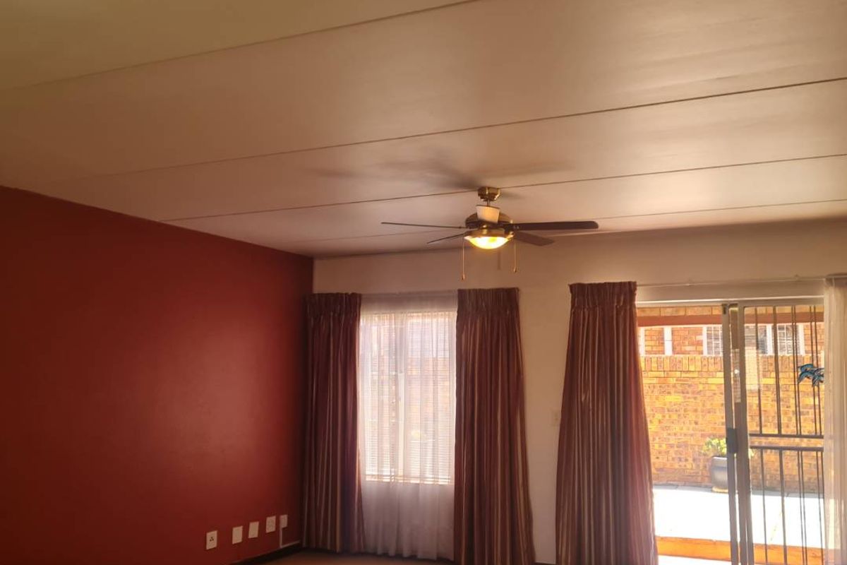 Spacious living area featuring a ceiling fan, carpeted flooring, and direct access to an outdoor patio through a sliding glass door with security gate.