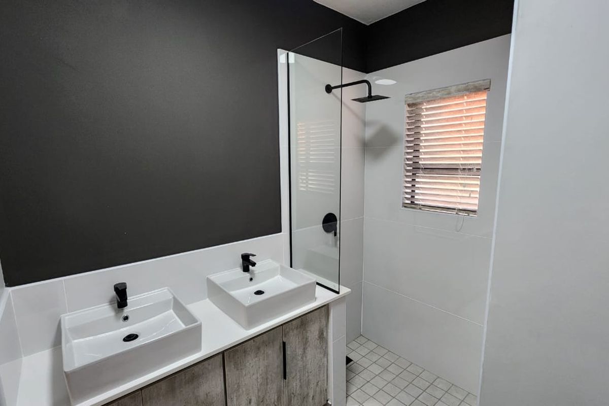 Modern bathroom featuring a double vanity with vessel sinks, a walk-in shower with a glass screen, and contemporary matte black fixtures.
