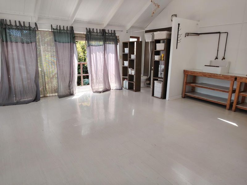 Open plan living area featuring vaulted ceilings with exposed rafters, light vinyl flooring, and a functional utility area with exposed plumbing and sink.