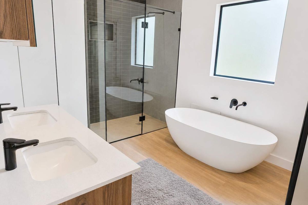 Modern bathroom featuring a double vanity with stone countertop, a freestanding bathtub, and a walk-in glass-enclosed shower with dark tiled accents.
