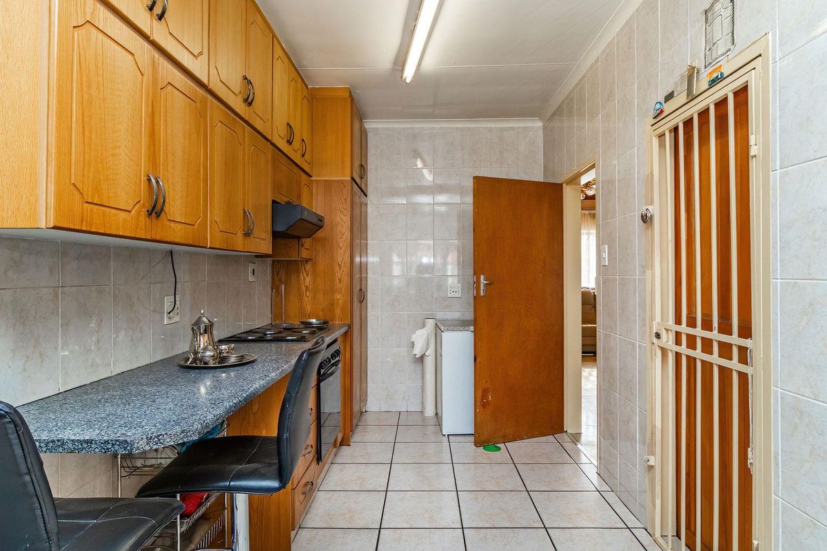A functional kitchen featuring built-in wooden cabinetry, a laminate countertop, integrated oven and hob, and fully tiled walls and floors.
