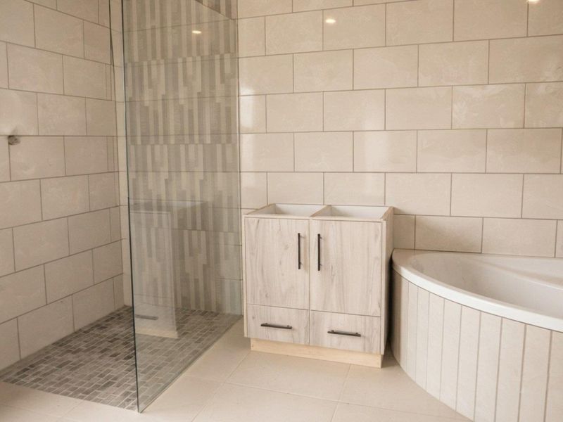 A modern bathroom featuring a walk-in shower with glass screen, tiled walls, and a built-in bathtub, currently awaiting vanity countertop and basin installation.