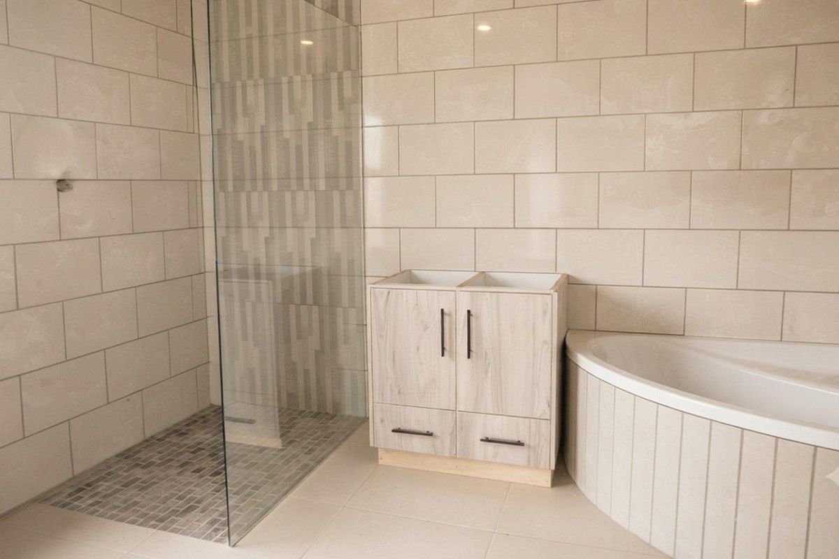 A modern bathroom featuring a walk-in shower with glass screen, tiled walls, and a built-in bathtub, currently awaiting vanity countertop and basin installation.