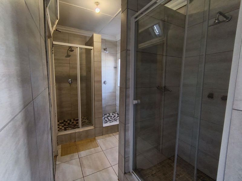 A functional bathroom featuring multiple walk-in shower enclosures with tiled finishes and neutral flooring.