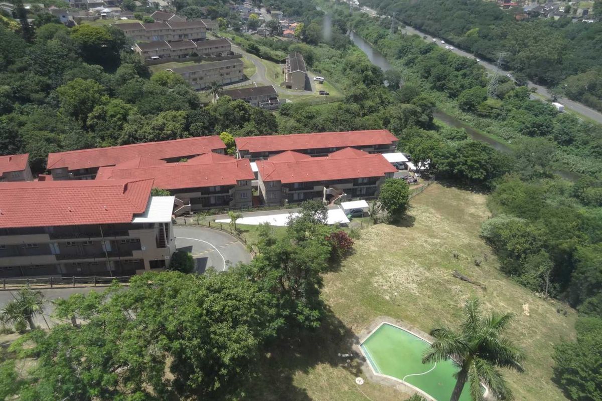 Aerial view of the apartment complex featuring multiple buildings with tiled roofs, a swimming pool, and surrounding green space.