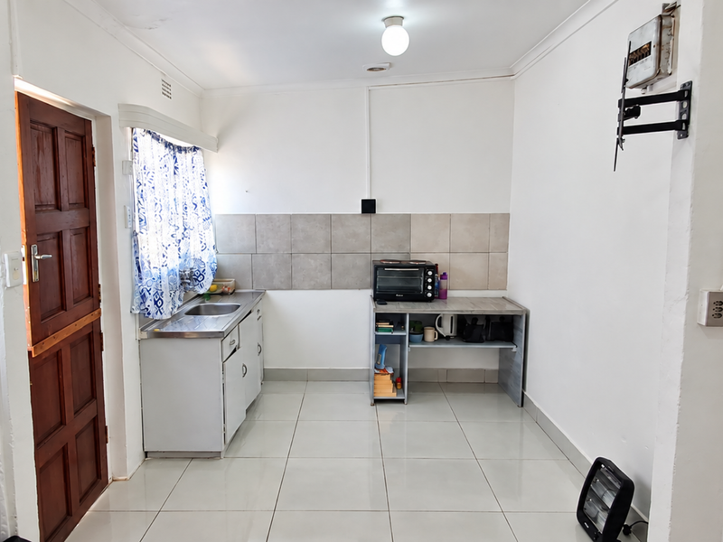 A compact kitchen area featuring tiled flooring, a stainless steel sink, and a tiled backsplash, offering a functional space ready for modernization.