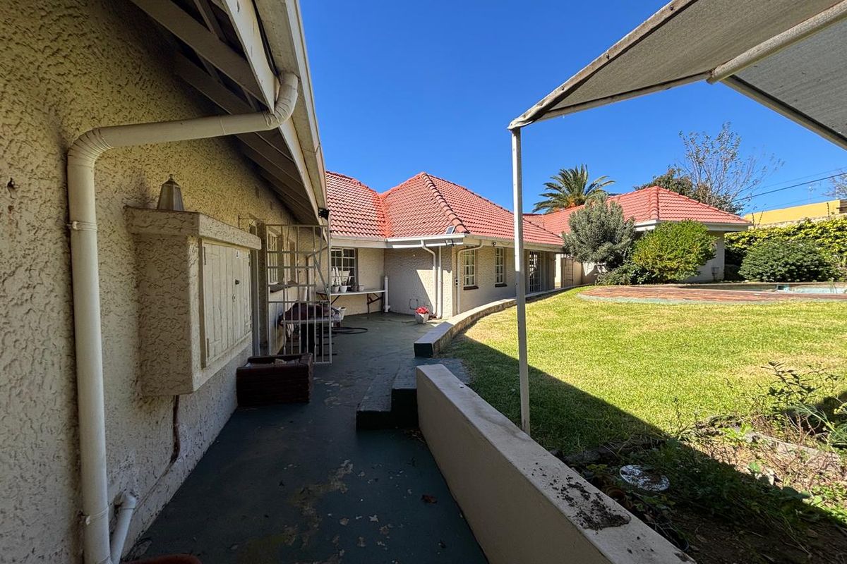 A rear exterior view of the house featuring a covered patio area, a lawn, and a retaining wall leading to the garden.
