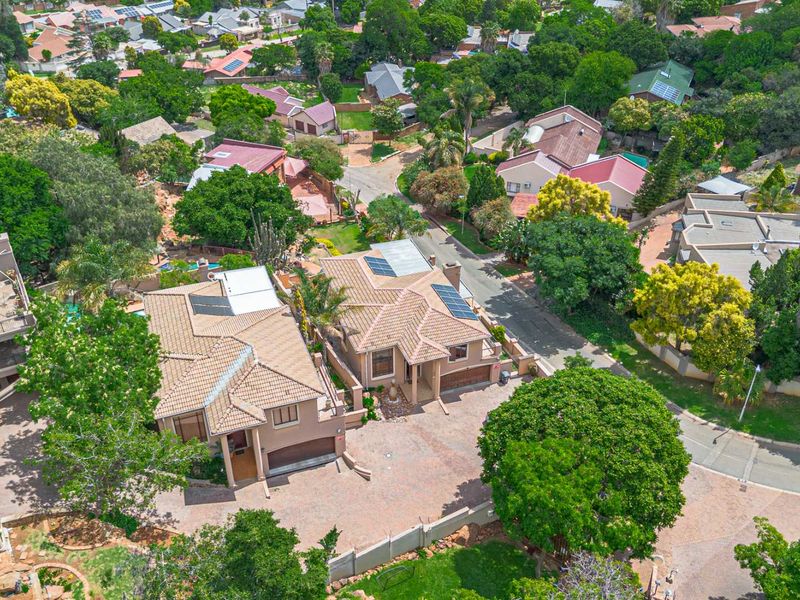 An aerial view of the residential property showing the tiled roof, solar panels, paved driveway, and surrounding landscaped neighbourhood.