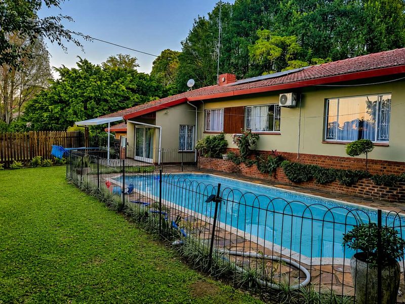 Rear exterior view of the property featuring a swimming pool, paved surround, and established garden area with a brick and plaster facade.