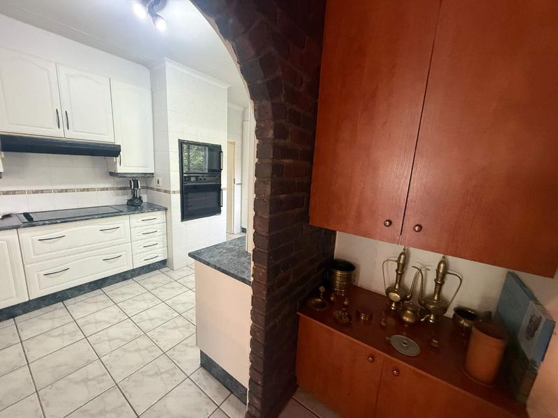 Kitchen featuring white cabinetry, built-in oven and microwave, dark countertops, and a distinctive brick archway leading to an adjacent storage or prep area.