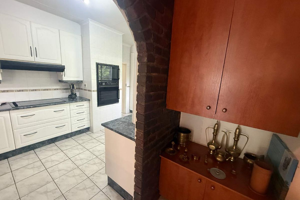 Kitchen featuring white cabinetry, built-in oven and microwave, dark countertops, and a distinctive brick archway leading to an adjacent storage or prep area.