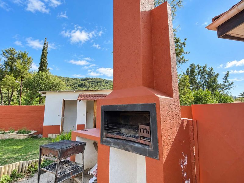 Outdoor entertainment area featuring a prominent built-in masonry braai and chimney, set within a private garden space.