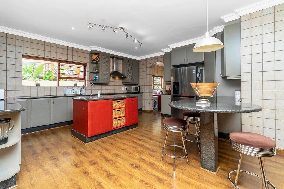 Spacious kitchen featuring a central red island, granite countertops, grey cabinetry, and integrated stainless steel appliances with wood-look flooring.