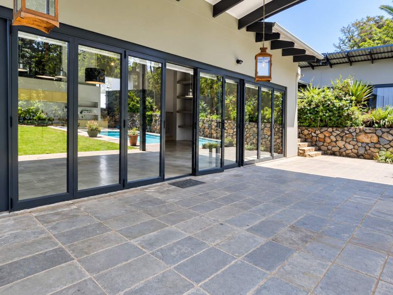 Spacious covered patio featuring large stacking glass doors, stone paving, and exposed timber rafters, offering seamless indoor-outdoor flow to the pool area.