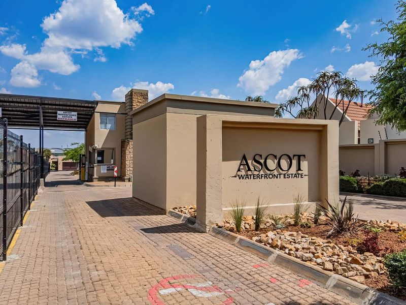 The entrance to Ascot Waterfront Estate featuring a paved driveway, security gate, and estate signage.