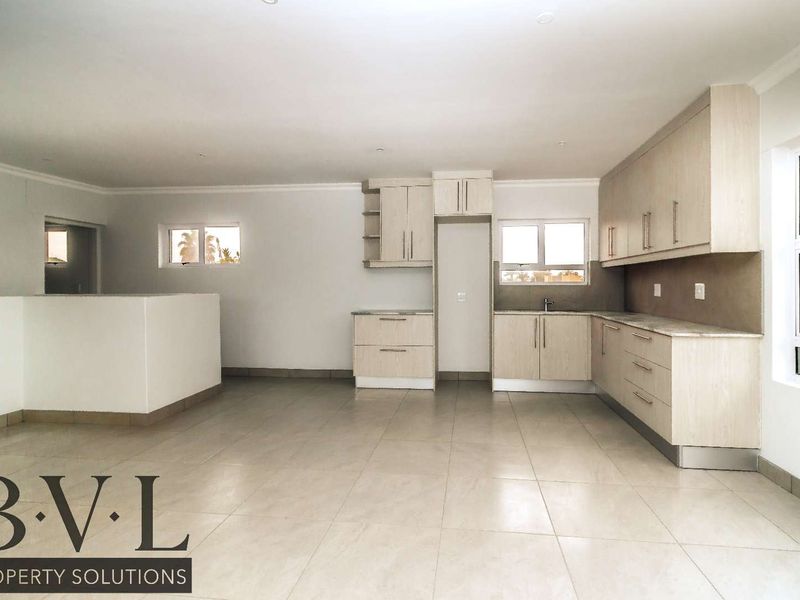 Spacious open-plan kitchen and living area featuring modern light-wood cabinetry, stone countertops, and neutral tiled flooring throughout.