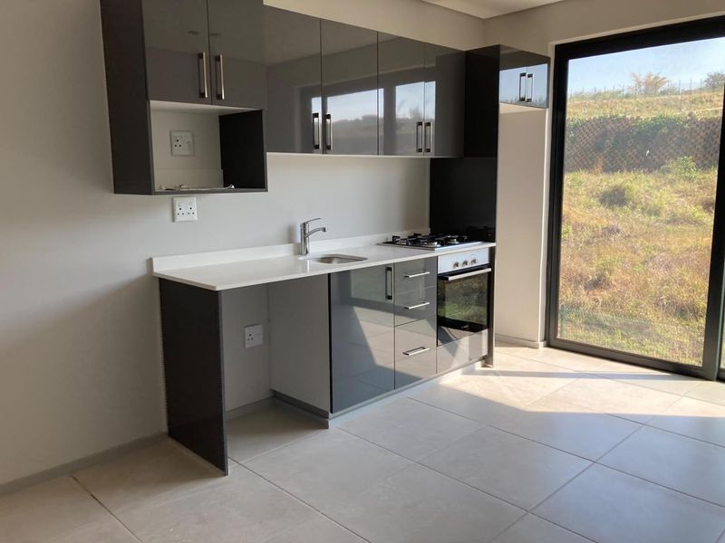 Modern kitchen featuring high-gloss cabinetry, stone countertops, integrated gas hob and oven, and direct access to the outdoors through a large sliding glass door.
