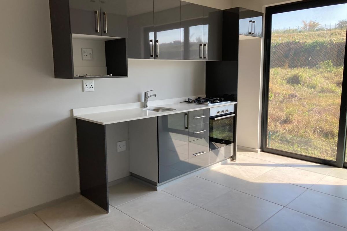 Modern kitchen featuring high-gloss cabinetry, stone countertops, integrated gas hob and oven, and direct access to the outdoors through a large sliding glass door.