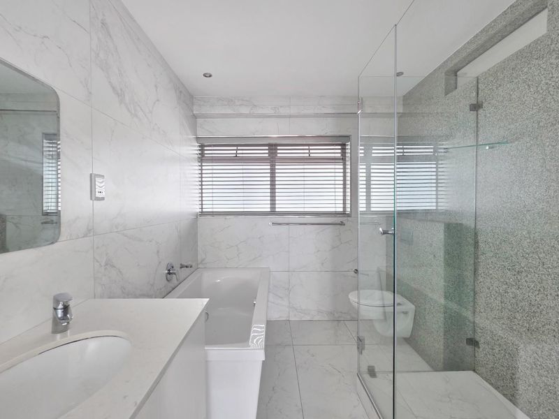 Modern bathroom featuring marble-look wall tiles, a built-in vanity, a bathtub, and a separate glass-enclosed shower with high-quality finishes.