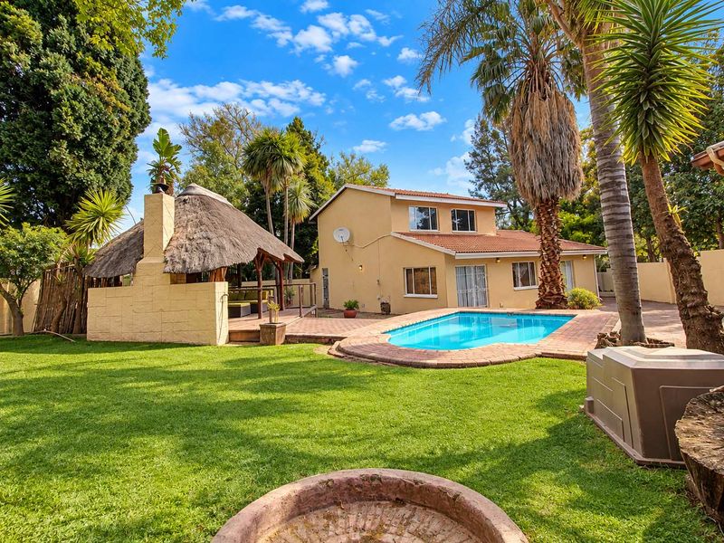 Spacious rear garden featuring a swimming pool, brick-paved patio area, and a traditional thatched lapa with a built-in braai.