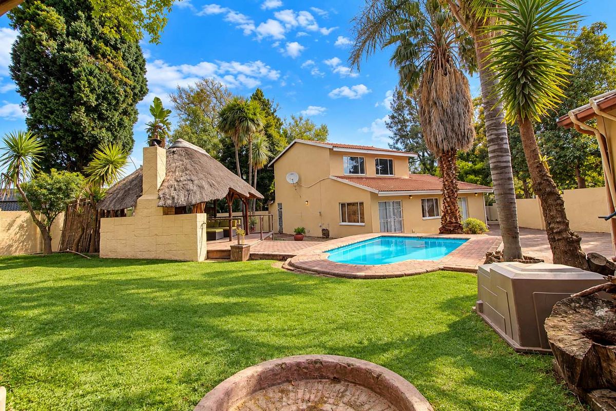 Spacious rear garden featuring a swimming pool, brick-paved patio area, and a traditional thatched lapa with a built-in braai.
